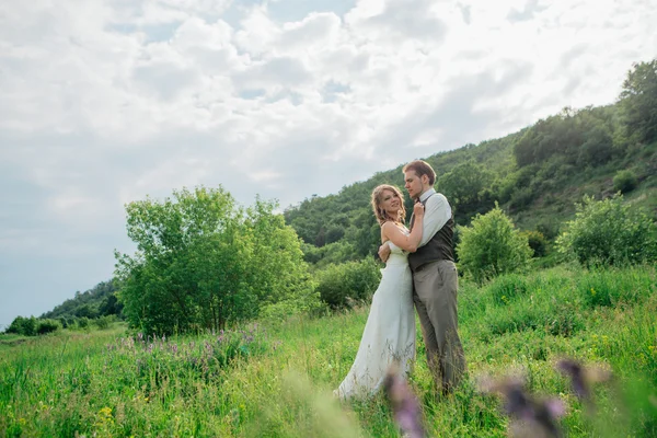 Das Brautpaar mit einem Strauß im Gras vor dem Hintergrund der Berglandschaft — Stockfoto