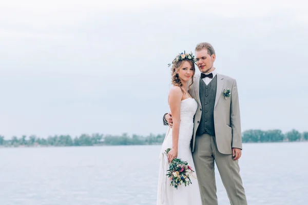 Unga brudgummen och bruden stående kramas på bakgrunden av floden — Stockfoto