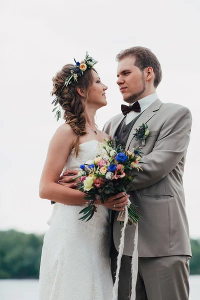 Young groom and bride standing hugging on the background of the river — Stock Photo, Image