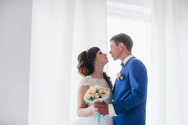 Bride and groom in studio light stand kiss on a white background — Stock Photo, Image