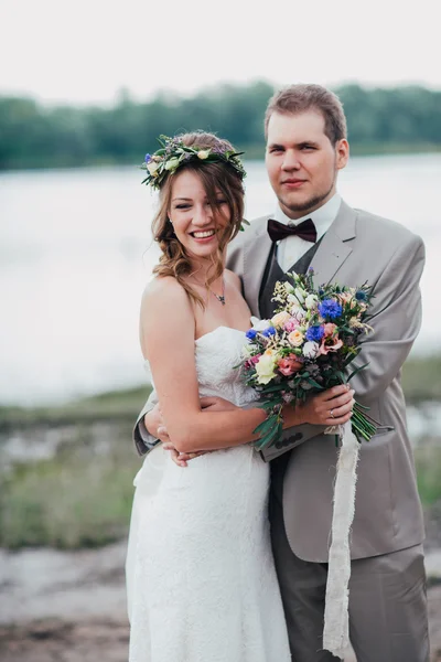 Unga brudgummen och bruden stående kramas på bakgrunden av floden — Stockfoto