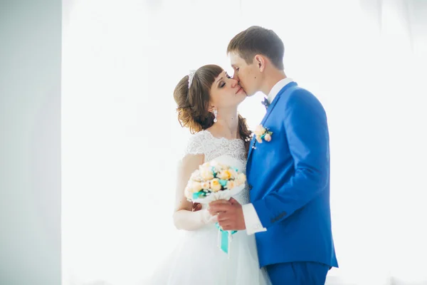 Bride and groom in studio light stand  kiss on a white background — Stock Photo, Image