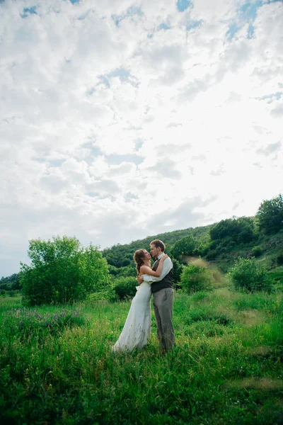 La mariée et le marié avec un bouquet dans l'herbe sur le fond paysage de montagne — Photo