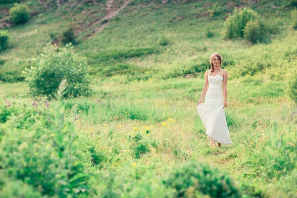 Bruden står på en bakgrund av gräs och berg — Stockfoto