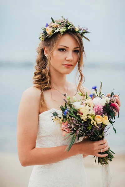 Joven novia con un ramo de flores de pie en el fondo del río — Foto de Stock