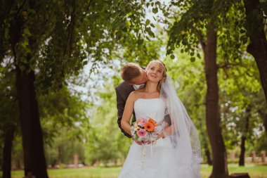 Gelin ve damat bir park kissing.couple yeni evli gelin ve damat doğa yeşil orman bir düğünde fotoğraf portre öpüşme. Düğün çift aşk