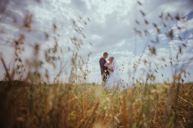 güzel gelin ve damat otların arasında duran ve öpüşme. Düğün çift moda çekimi.