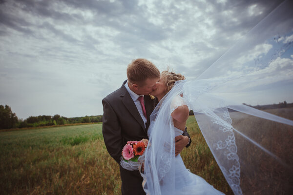 Beautiful bride and groom standing in grass and kissing. Wedding couple fashion shoot.