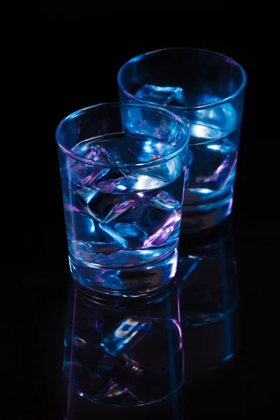 Två glas vodka med isbitar mot bakgrund av djupa blå glöd. — Stockfoto