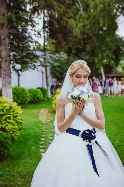 Novia en un vestido blanco en el parque verde de verano con un ramo en la mano — Foto de Stock