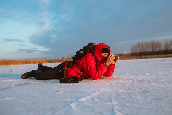 Фотограф фотографирует на берегу реки зимой — стоковое фото