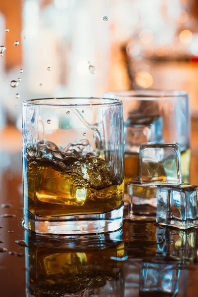 Vaso de whisky con hielo y luz cálida sobre mesa negra con reflexión, ambiente cálido —  Fotos de Stock