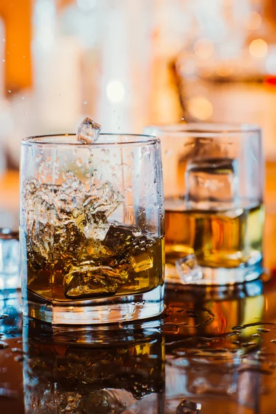 Vaso de whisky con hielo y luz cálida sobre mesa negra con reflexión, ambiente cálido — Foto de Stock