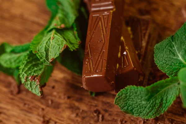 stack of chocolate pieces with a leaf of mint on wooden background