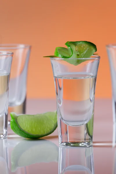 Tequila sparato con una fetta di lime sullo sfondo arancione vetro — Foto Stock