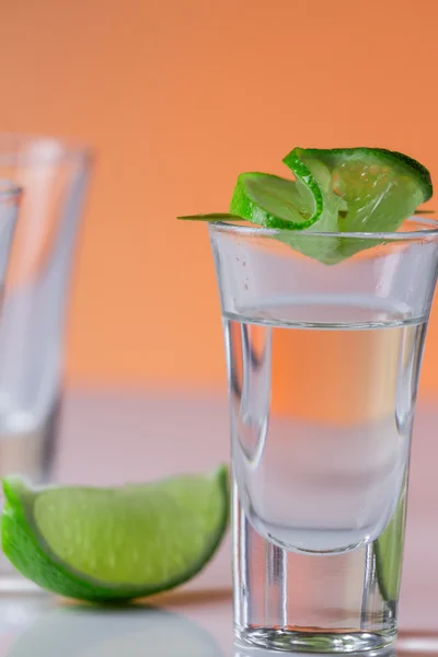 Tequila shot with a slice of lime on the glass orange background — Stock Photo, Image