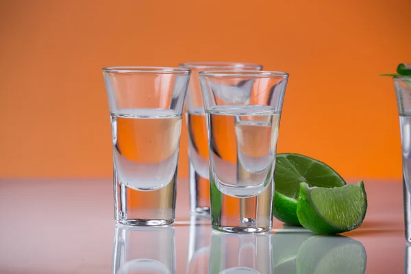 Tequila shot with a slice of lime on the glass orange background — Stock Photo, Image