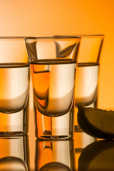 Tequila shot with a slice of lime on the glass orange background — Stock Photo, Image