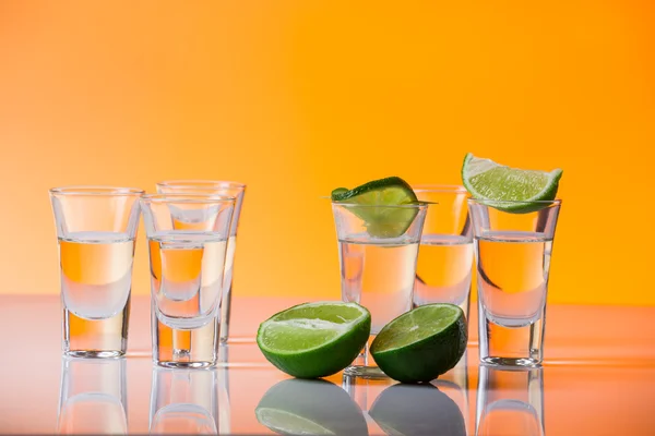 Tequila sparato con una fetta di lime sullo sfondo arancione vetro — Foto Stock