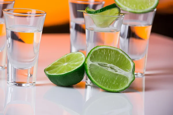 Tequila sparato con una fetta di lime sullo sfondo arancione vetro — Foto Stock