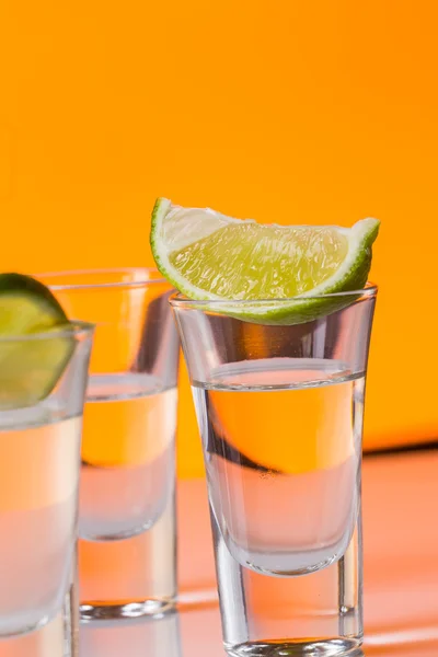 Tequila shot with a slice of lime on the glass orange background — Stock Photo, Image