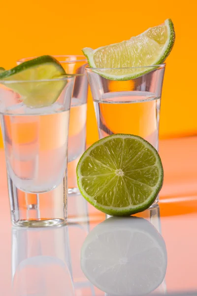 Tequila Shot mit einer Scheibe Limette auf dem orangefarbenen Hintergrund — Stockfoto