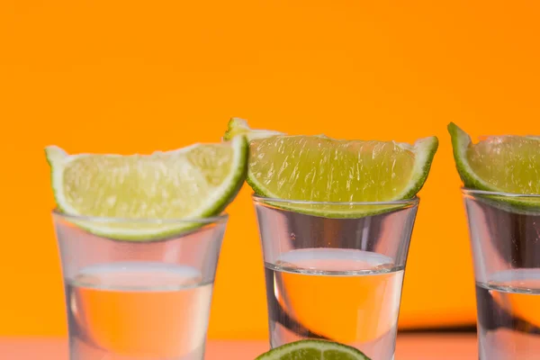 Tequila sparato con una fetta di lime sullo sfondo arancione vetro — Foto Stock