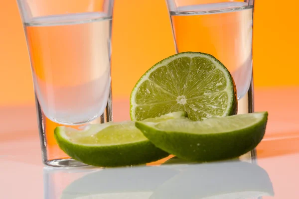 Tequila sparato con una fetta di lime sullo sfondo arancione vetro — Foto Stock