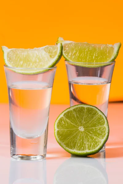 Tequila shot with a slice of lime on the glass orange background — Stock Photo, Image