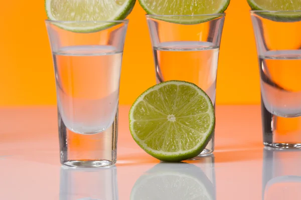 Tequila Shot mit einer Scheibe Limette auf dem orangefarbenen Hintergrund — Stockfoto