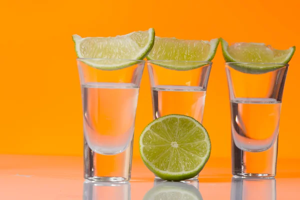 Tequila Shot mit einer Scheibe Limette auf dem orangefarbenen Hintergrund — Stockfoto