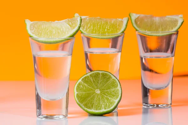 Tequila shot with a slice of lime on the glass orange background — Stock Photo, Image