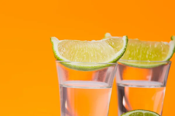 Tequila sparato con una fetta di lime sullo sfondo arancione vetro — Foto Stock