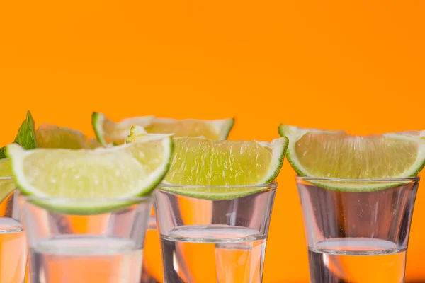 Tequila shot s plátkem limetky na sklo oranžové pozadí — Stock fotografie