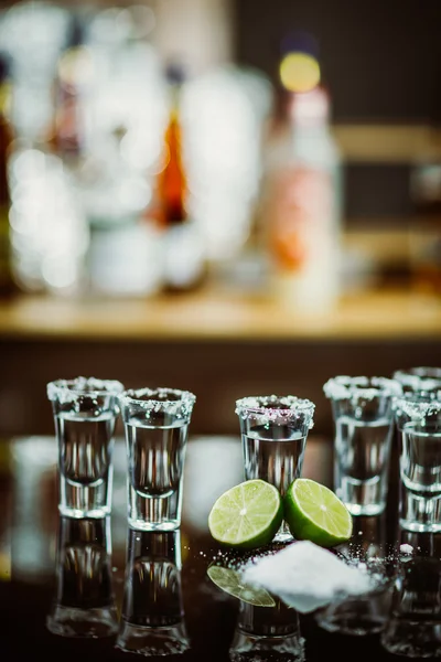 Két lövés a mész és a sóval, egy fából készült asztal bár a háttérben az élénk fények, bár a tequila — Stock Fotó