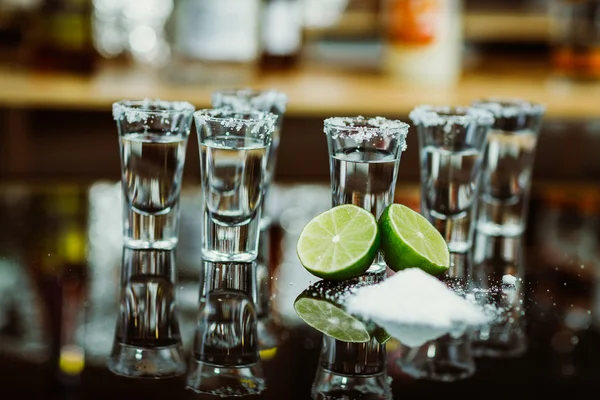 Két lövés a mész és a sóval, egy fából készült asztal bár a háttérben az élénk fények, bár a tequila — Stock Fotó