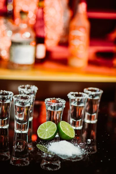 Due bicchierini di tequila con lime e sale su un tavolino di legno bar sullo sfondo di luci brillanti del bar — Foto Stock