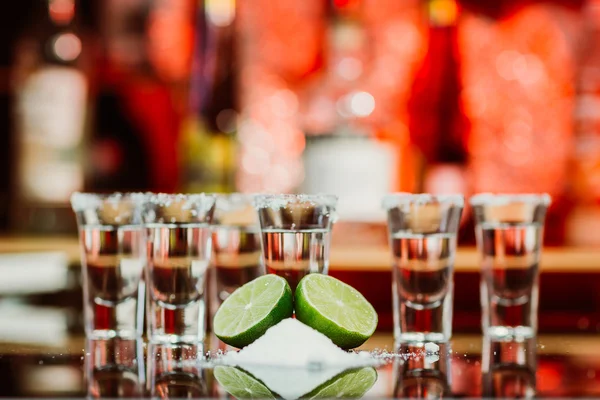 Dos chupitos de tequila con lima y sal en una barra de madera en el fondo de luces brillantes de la barra — Foto de Stock