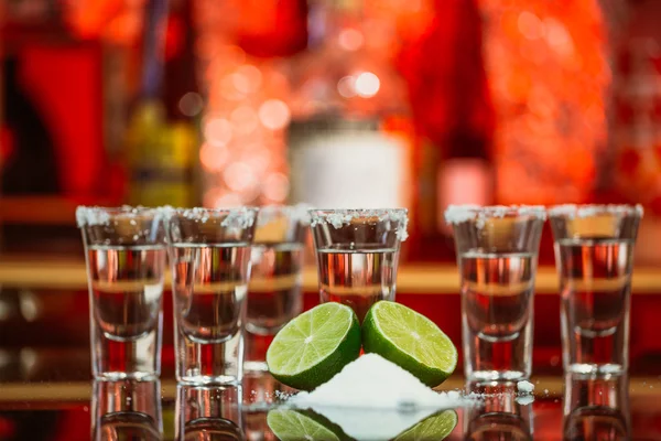 Dos chupitos de tequila con lima y sal en una barra de madera en el fondo de luces brillantes de la barra — Foto de Stock