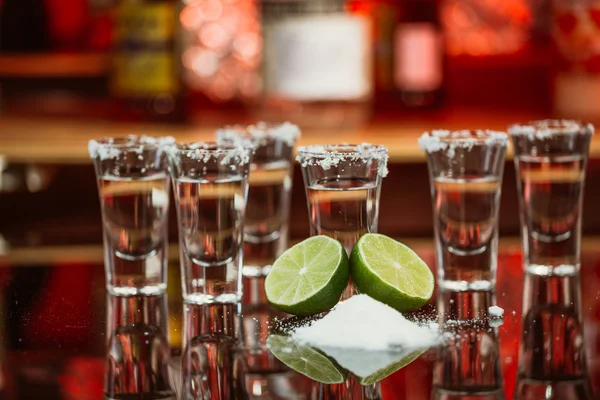 Dos chupitos de tequila con lima y sal en una barra de madera en el fondo de luces brillantes de la barra — Foto de Stock