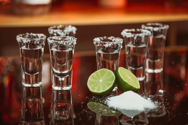 two shots of tequila with lime and salt on a wooden table bar on the background of bright lights of the bar