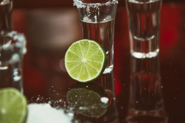 Dos chupitos de tequila con lima y sal en una barra de madera en el fondo de luces brillantes de la barra —  Fotos de Stock