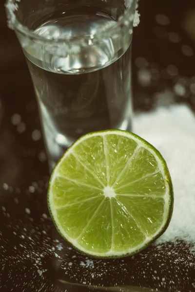 Due bicchierini di tequila con lime e sale su un tavolino di legno bar sullo sfondo di luci brillanti del bar — Foto Stock