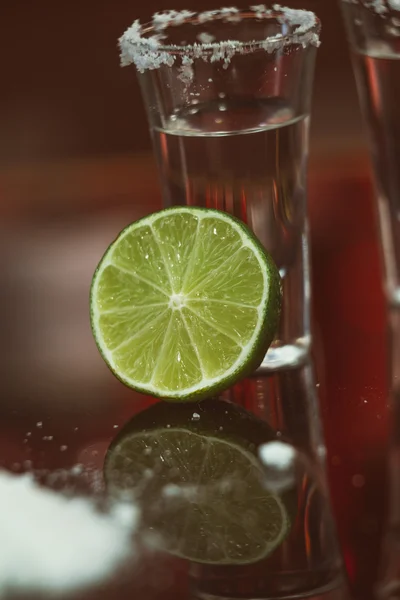 Due bicchierini di tequila con lime e sale su un tavolino di legno bar sullo sfondo di luci brillanti del bar — Foto Stock