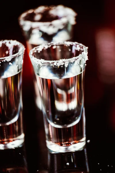 Dos chupitos de tequila con lima y sal en una barra de madera en el fondo de luces brillantes de la barra — Foto de Stock