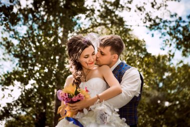 mutlu gelin, yeşil park, ayakta damat öpüşme, gülüyor, gülüyor. düğün günü severler. 