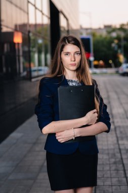 Successful businessman, standing against the backdrop of buildings holding  folder with sales charts. City business woman working.