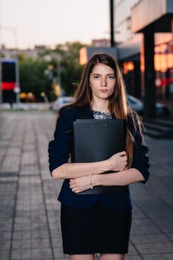 Successful businessman, standing against the backdrop of buildings holding  folder with sales charts. City business woman working.