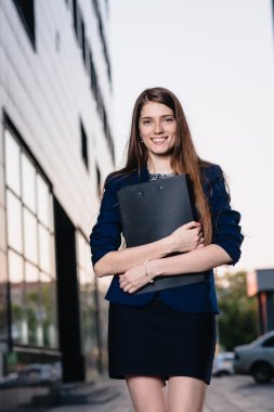 Successful smiling businessman, standing against the backdrop of buildings holding  folder with sales charts. City business woman working.