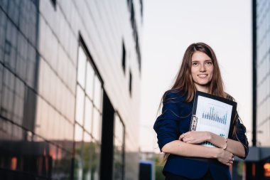 Successful smiling businessman, standing against the backdrop of buildings holding  folder with sales charts. City business woman working.